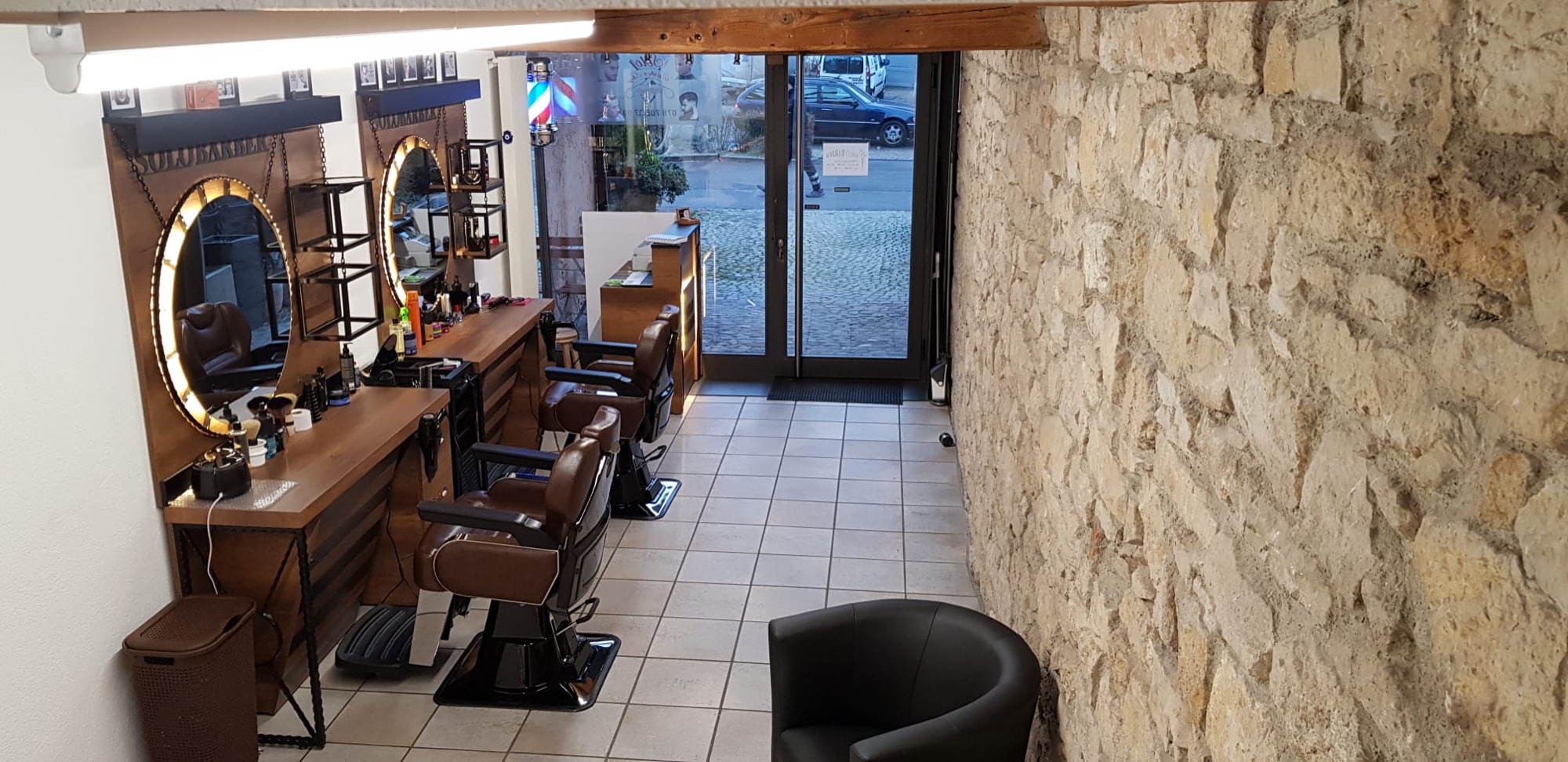 Blick durch den Salon mit Natursteinwand, Barberstühlen und Eingang zur Hauptstrasse